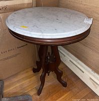 Front and top view of vintage wooden side table with round marble top placed on wooden floor next to cardboard boxes.
