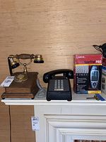 Wide shot of three items on shelf: vintage rotary telephone, black push-button phone, and SporTrak Pro GPS in box.