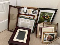 Wide view of grouped picture frames stacked and leaning against wall, showing variety of frame styles and sizes