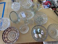 Fourteen assorted pieces of cut glass and crystal including bowls, vases, and decorative glass eggs on a table.