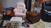 Pink cushioned white wooden glider chair with matching ottoman and vintage dark wooden side table cabinet on a patterned carpet.