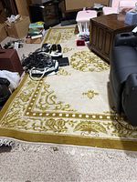 Full view of the large Asian style area rug under furniture and clutter, showing general design, color palette, and fringed edge.