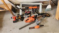 Photo showing multiple garden tools on a concrete floor including cordless drill, hedge trimmers, and weed whacker