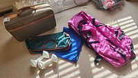 Photo showing vintage Hartmann suitcase, pink/black duffel bag, teal bag, blue fabric item, and pair of white hand weights on carpet with sunlight.