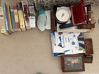 Overall view of lot showing books, a tissue box, a plastic organizer, ream of printer paper, CDs on spindle, eyeglass case, wallet/pouch, and framed picture.