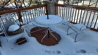 Full view of patio set on deck covered with snow, showing round table, loveseat, 3 chairs.