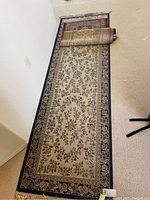 Long runner rug with beige background, floral detailing, floral border, partially rolled at one end.