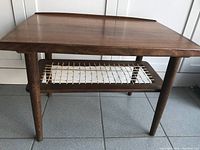 Angle view showing two tiers of the table with walnut top including raised edges and rattan lower shelf.