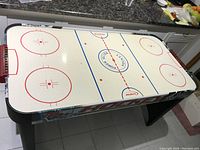 Full view of the air hockey table showing the white surface with ice-hockey rink markings and black legs.