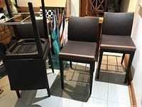 Photo showing four black faux leather bar chairs with wooden frames, with one chair placed upside down showing the underside structure.