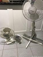 Front view of three fans: one large standing fan and two smaller tabletop fans on the floor in front of a cabinet