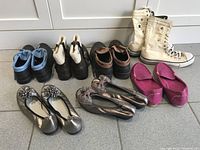 Seven pairs of women's shoes of various styles and colors arranged on floor.