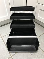 Open black multi-tier makeup case showing four expandable trays inside a silver aluminum exterior.