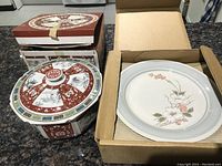Boxed Asian patterned serving bowl with lid, alongside boxed white floral plates.