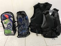 Two mesh bags with snorkel gear at left, two black neoprene vests at right