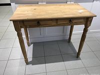 Front view of wood table showing entire item with two drawers and turned legs.