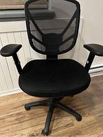 Front view of the black Staples task chair showing the cushioned seat with mesh backrest and armrests.