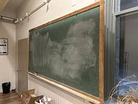 Photo showing the full length of the large vintage schoolhouse blackboard mounted on a classroom wall with the chalk surface partly erased and free of major damage.