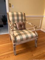 Front angle view of the accent chair showing checkered beige and sage upholstery with visible carved wooden arms and legs, and mauve decorative pillow on the seat.