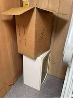 Box labeled 'GLASS' on top of an off-white cabinet, implying one cabinet is new and boxed and the other is unpacked.