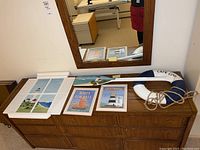 Photo showing full set of nautical wall decor arranged on table beneath mirror: lighthouse window, two framed prints, life ring, and wooden oar.