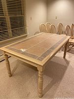Full angled view of the wood dining table with tile decor, showing entire table with light wood frame and legs in a room with chairs around.