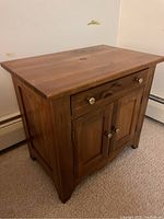 Wood nightstand angled front view showing top surface, drawer, cabinet doors, and brass knobs.
