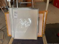 Set of four picture frames stacked, showing both silver metallic and gold-colored wooden frames with one frame containing architectural prints.