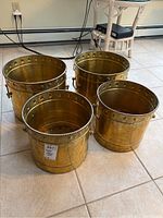 Four brass pots arranged in pairs by size on tile floor, showing overall condition, tarnishing, and shape
