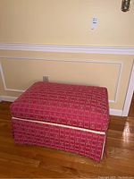 Front view of rectangular red upholstered ottoman with geometric pattern and pleated skirt.