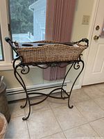 Full side view of wrought iron plant stand with woven wicker basket and green glass accents on handles.