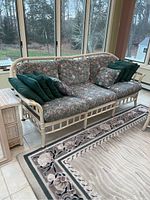 Off-white rattan sofa with floral patterned cushions and solid green accent pillows shown from the front angle in a sunroom.