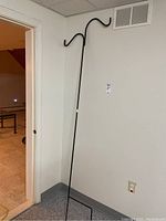 Full view of the tall black metal shepherd's hook leaning against a white wall near a doorway