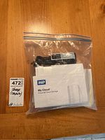 Plastic bag containing WD My Cloud manual and power adapter on top of a wooden table.
