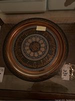 Full view of the round metal tray showing entire decorative pattern including copper inlay, script, and outer border.