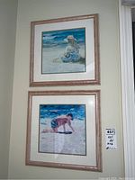 Two framed and matted pictures depicting children at the beach, hung on a cream wall.