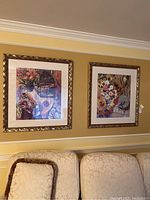 Pair of two matching wall art pieces in gold carved frames hanging side by side on a wall above cream textured couches.