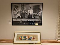 Black and white framed 'The Rat Pack' poster above colorful framed bird wall art on wood surface next to wall.