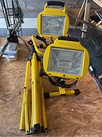 View of two Workforce brand yellow work lights mounted on foldable yellow metal tripod stands, showing overall lot contents.