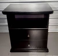 Front view of the black wooden nightstand showing two drawers with silver knobs and an open shelf above the drawers.