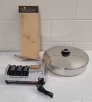 Pampered Chef mandolin in original box, large stainless steel saucepan with lid, and Chef's Choice electric knife sharpener with three slots and power cord.