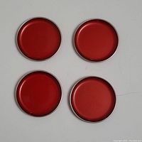 Top view showing four round red enamel coasters with smooth glossy surfaces and metal rims.