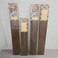 Four packages of Impact wall shelves by Barclay standing upright unopened against a wall. Three packages are significantly taller (56") than one (44").