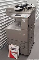 Front view of Canon multifunction printer on wheels with manuals on floor