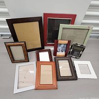 Full lot of 10 mixed picture frames arranged on a table showing various sizes and styles including wood and metal frames.