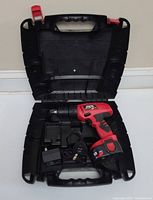 Opened black plastic carrying case containing red and black Skil cordless drill with attached battery pack, battery charger and power cable inside.
