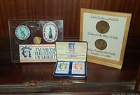 Complete collection of Statue of Liberty themed collectibles on a wooden surface including framed coins, playing cards, coins, and emblems