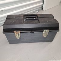 Closed black plastic toolbox with metal latches and carry handle on top.