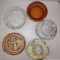 Top-down photo showing the five vintage ashtrays, varying materials and colors, arranged on white surface.