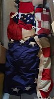 Folded and piled four vintage American flags showing red and white stripes and blue fields with white stars. Flags are in various sizes and fabric condition shows vintage wear.